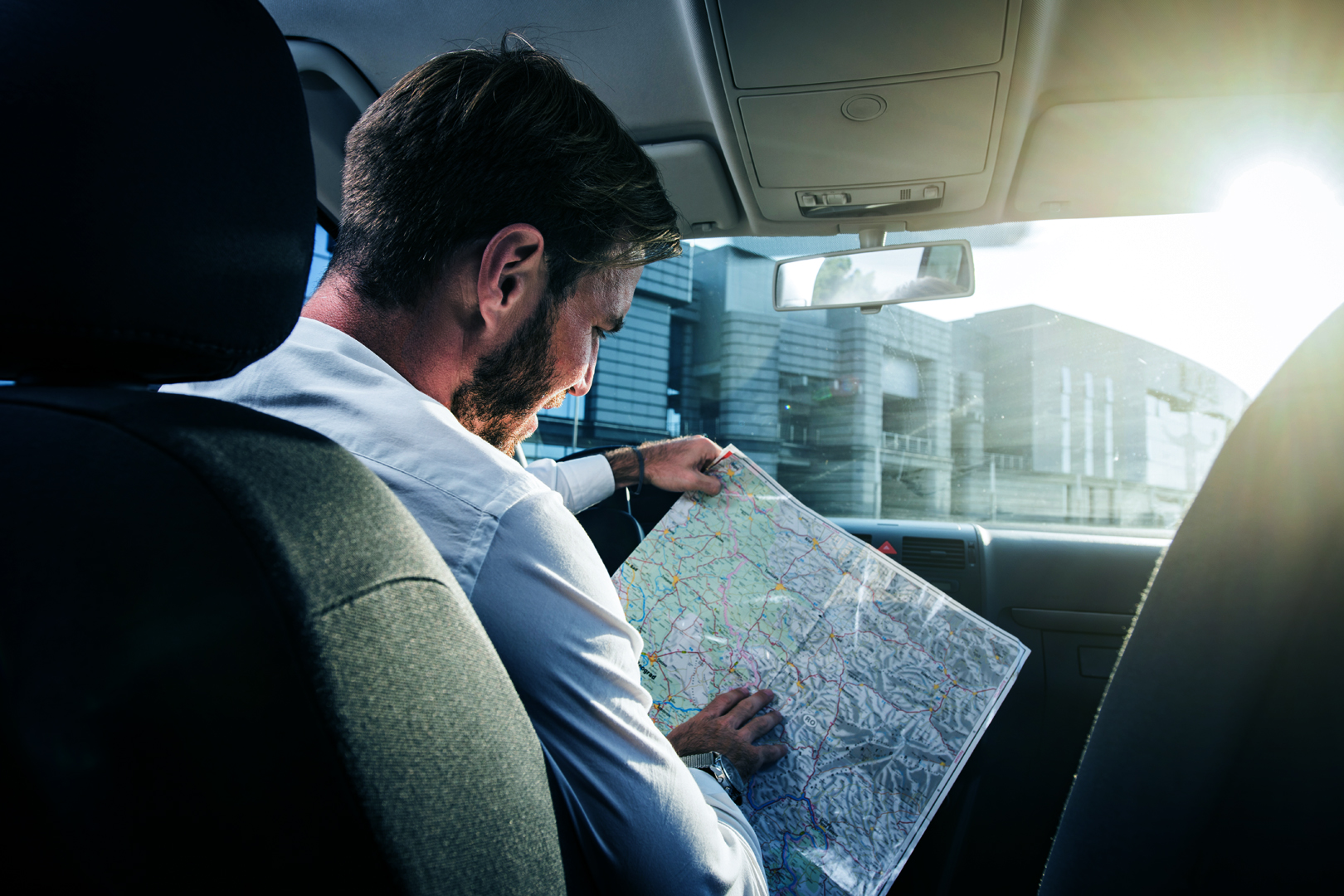 Professional in a car passenger seat studying a paper road map by sunlight, symbolizing navigating a career path without GPS.