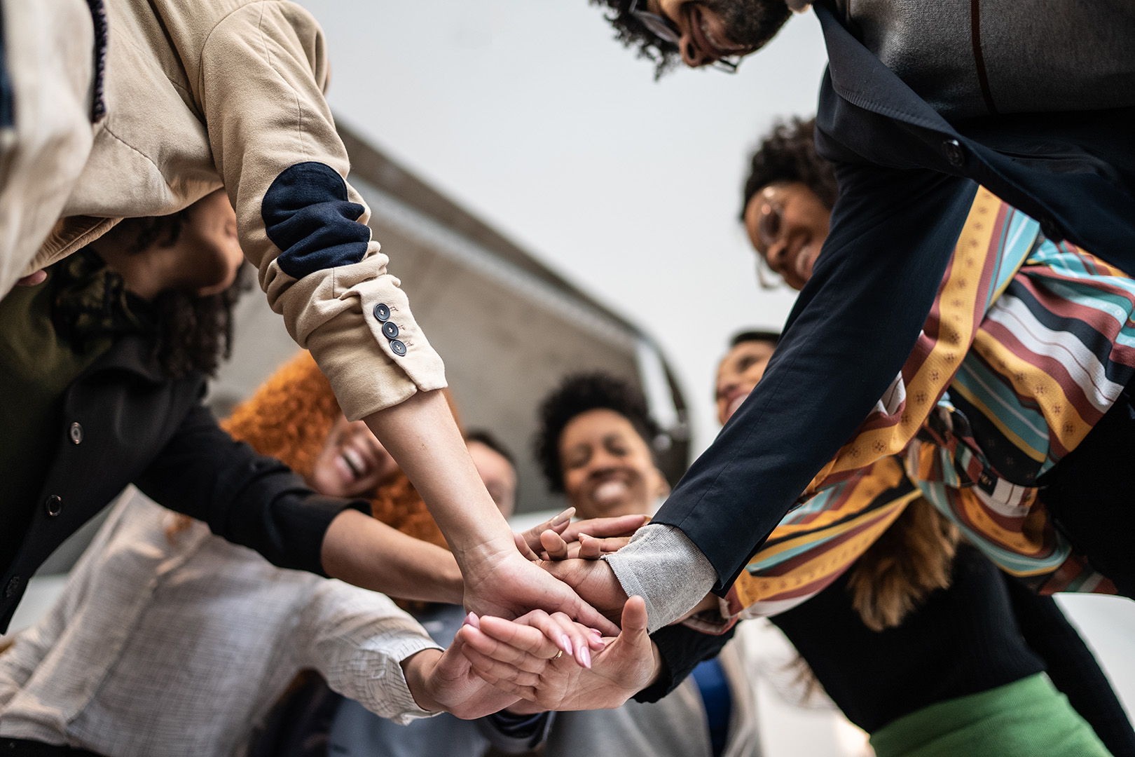 Group of diverse professionals smiling and stacking hands together in a gesture of teamwork and collaboration.