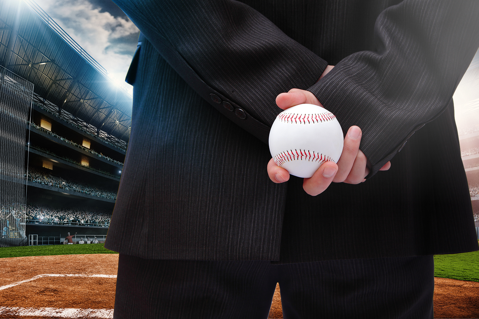 A photo of person in a suit standing in a baseball stadium, focused on their hands holding a baseball.