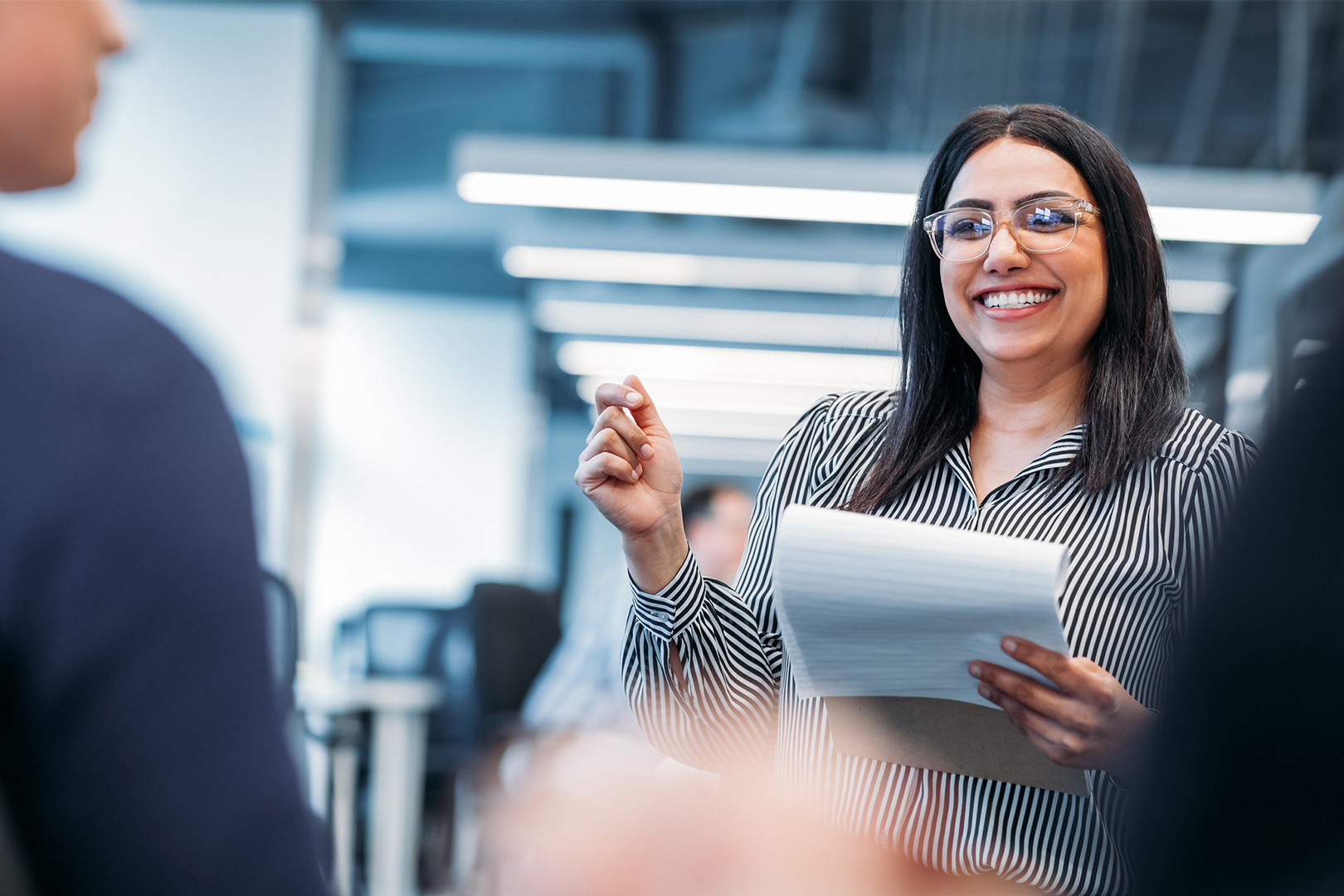 A woman smiling, holding a clipboard, and addressing a fellow coworker.
