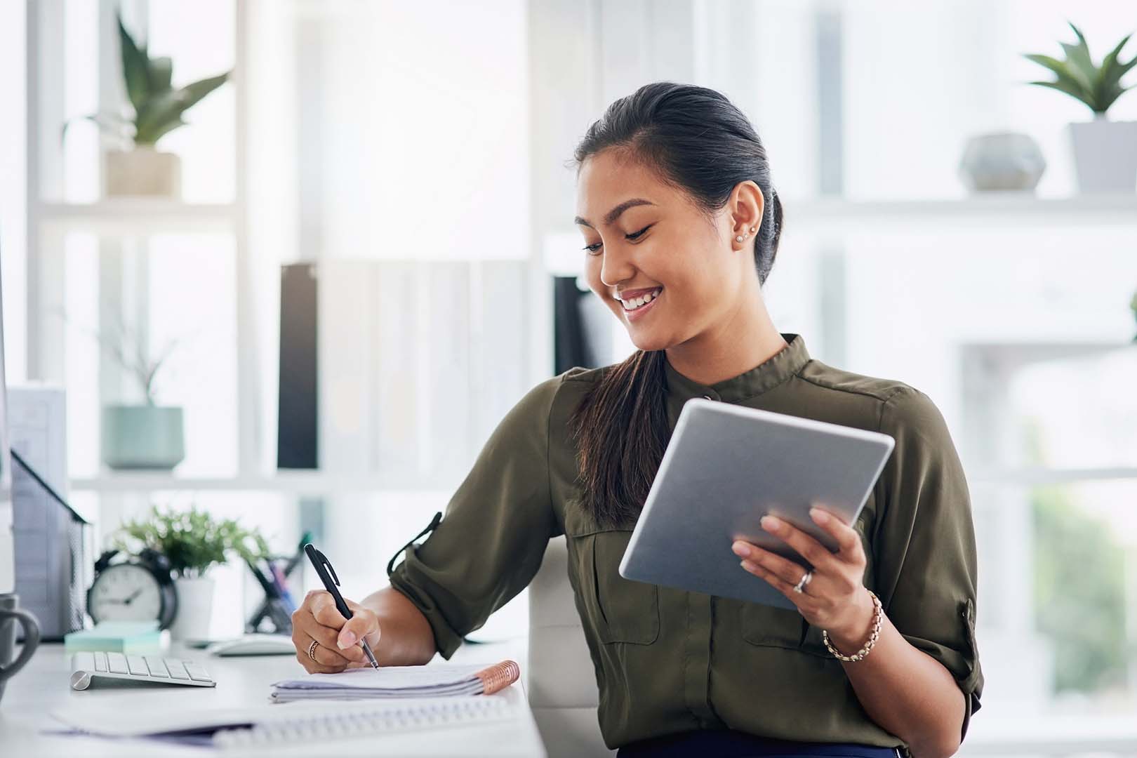 A woman holding a tablet and writing on a notepad