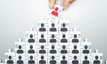 A hand working on a puzzle with silhoutettes of people on the pieces